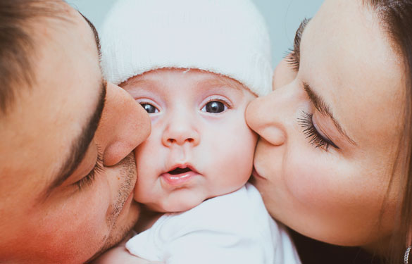 Adoptive parents kiss their new child on the cheek